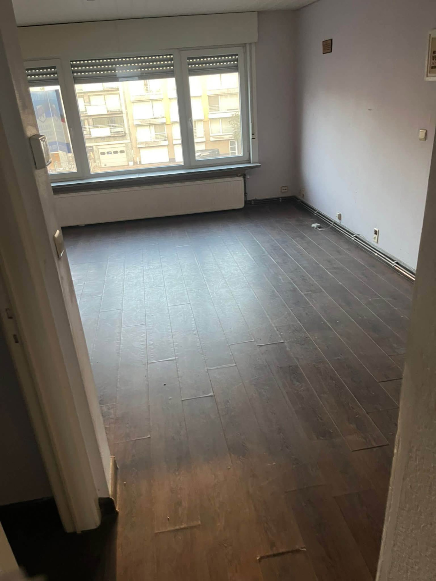 Studio na volledige leegmaking in Knokke: lege woonruimte met donkere vloer en vrijgemaakt raam