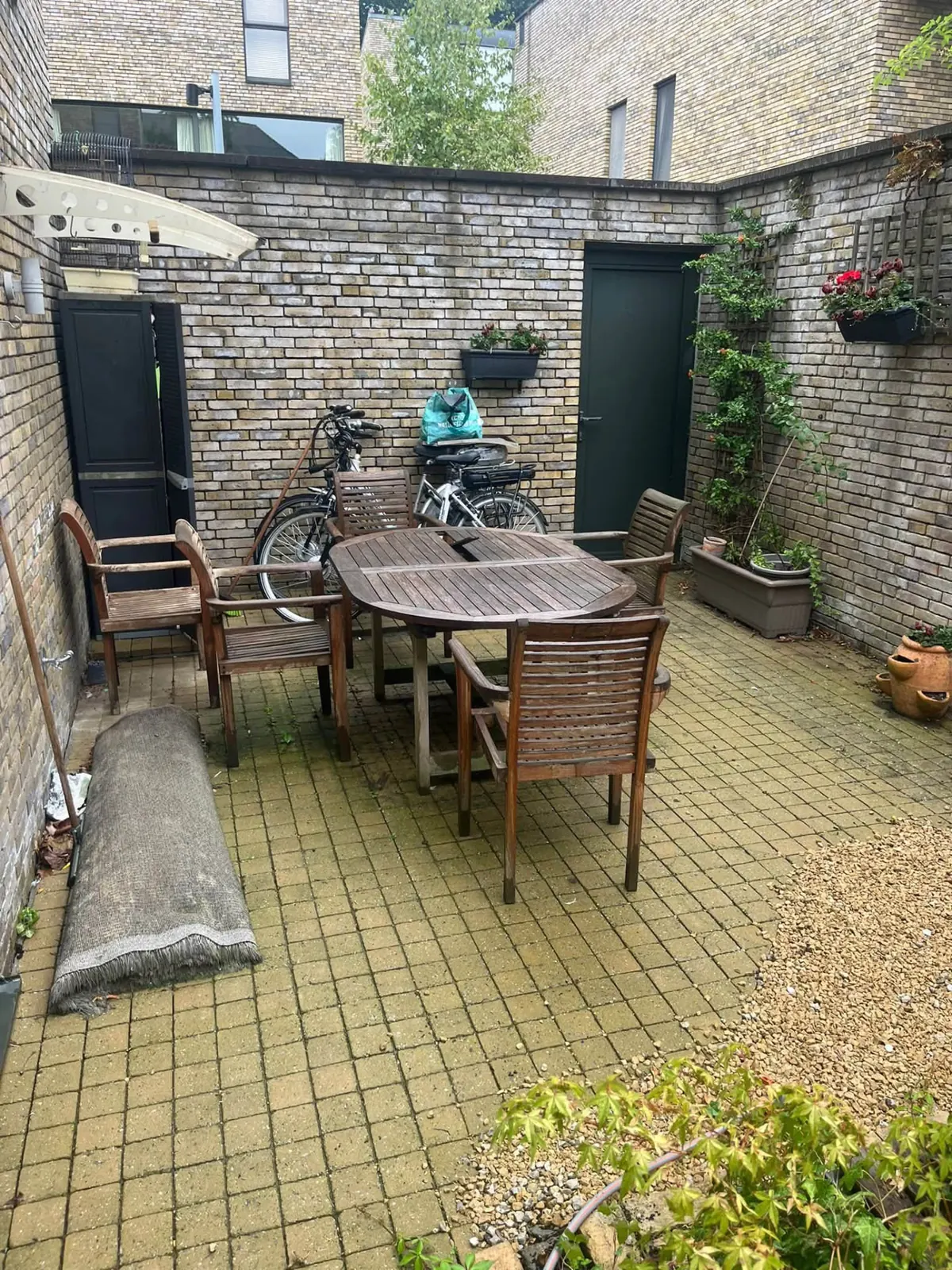 Buitenruimte met tuinset, fietsen en opgerold tapijt vóór de opruiming van de woning in Brugge